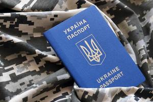 Ukrainian foreign passport on fabric with texture of military pixeled camouflage. Cloth with camo pattern in grey, brown and green pixel shapes and Ukrainian ID photo