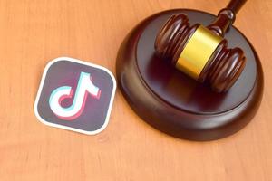 KHARKOV, UKRAINE - MAY 12, 2022 Tiktok paper logo lies with wooden judge gavel. Entertainment lawsuit concept photo