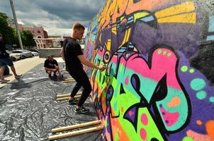 KHARKOV, UKRAINE - MAY 27, 2022 Festival of street arts. Young guys draw graffiti on portable wooden walls in the center of the city. The process of painting on walls with aerosol spray cans photo