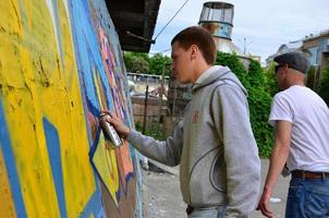 KHARKOV, UKRAINE - MAY 27, 2022 Festival of street arts. Young guys draw graffiti on an old concrete walls in the center of the city. The process of painting on walls with aerosol spray cans photo