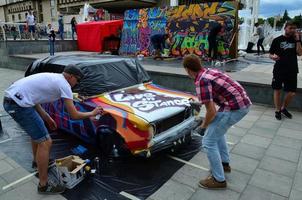 KHARKOV. UKRAINE - MAY 2, 2022 Festival of street art. Young guys draw graffiti on the car body in the city center. The process of drawing color graffiti on a car with aerosol cans photo