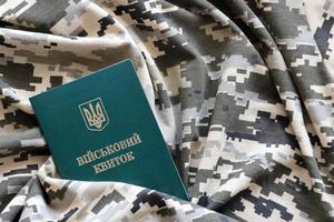 Ukrainian military ID on fabric with texture of pixeled camouflage. Cloth with camo pattern in grey, brown and green pixel shapes with Ukrainian army personal token photo