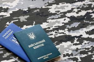 Ukrainian military ID and foreign passport on fabric with texture of pixeled camouflage. Cloth with camo pattern in grey, brown and green shapes with Ukrainian army personal token and passport. photo