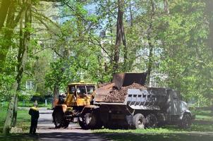 el equipo de mejora de la ciudad quita las hojas caídas en el parque con una excavadora y un camión. trabajo estacional regular en la mejora de los lugares públicos para la recreación foto