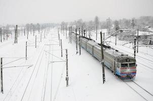 un largo tren de turismos se mueve a lo largo de la vía férrea. paisaje ferroviario en invierno después de la nevada foto