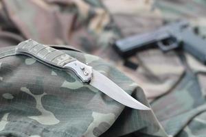 cuchillo táctico y pistola sobre tela verde camuflaje foto