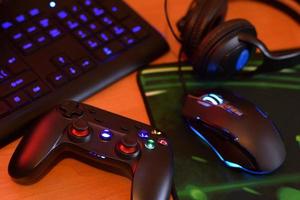 el gamepad moderno y el mouse para juegos se encuentran con el teclado y los auriculares en la mesa en la escena oscura de la sala de juegos. juguemos videojuegos juntos con el concepto de amigos foto