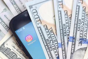 kharkov, ucrania - 3 de mayo de 2022 pantalla de teléfono inteligente con aplicación de instagram y muchos billetes de cien dólares. concepto de negocios y redes sociales foto