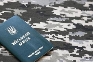 Ukrainian military ID on fabric with texture of pixeled camouflage. Cloth with camo pattern in grey, brown and green pixel shapes with Ukrainian army personal token photo