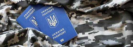 Ukrainian foreign passport on fabric with texture of military pixeled camouflage. Cloth with camo pattern in grey, brown and green pixel shapes and Ukrainian ID photo