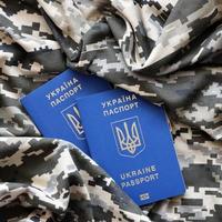 Ukrainian foreign passport on fabric with texture of military pixeled camouflage. Cloth with camo pattern in grey, brown and green pixel shapes and Ukrainian ID photo