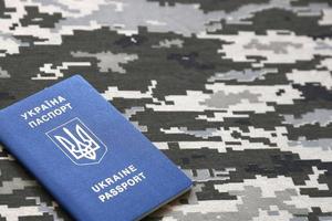 Ukrainian foreign passport on fabric with texture of military pixeled camouflage. Cloth with camo pattern in grey, brown and green pixel shapes and Ukrainian ID photo