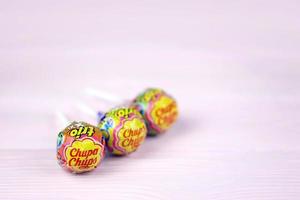 KHARKOV. UKRAINE - MAY 17, 2022 Chupa Chups products on pastel pink wooden table. Chupa Chups is a Spanish brand of lollipop and other confectionery founded in 1958 by Enric Bernat photo