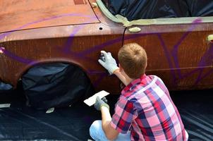 KHARKOV. UKRAINE - MAY 2, 2022 Festival of street art. Young guys draw graffiti on the car body in the city center. The process of drawing color graffiti on a car with aerosol cans photo