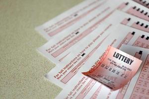 Red lottery ticket lies on pink gambling sheets with numbers for marking to play lottery. Lottery playing concept or gambling addiction. Close up photo