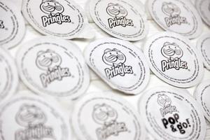 KHARKOV, UKRAINE - MAY 5, 2022 Pringles logo on paper membranes on white wooden table. Pringles is a brand of potato snack chips owned by Kellogg Company photo