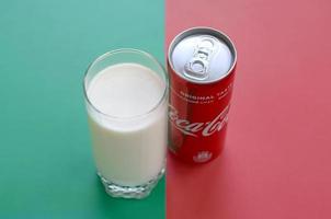 KHARKOV. UKRAINE - MAY 2, 2022 Coca cola red tin can and cup of fresh milk on red and green background surface photo