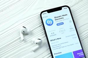 KHARKOV. UKRAINE - MAY 2, 2022 Shazam icon and application from App store on iPhone 12 pro display screen with airpods pro on white table photo