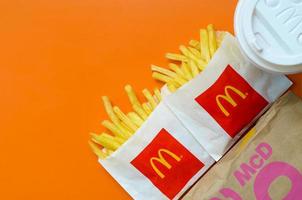 KHARKOV, UKRAINE - MAY 12, 2022 McDonald's French fries in small paperbag and coffee cup on bright orange background photo