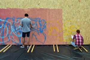 KHARKIV, UKRAINE - 20 MAY, 2022 Festival of street arts. Young guys draw graffiti on portable wooden walls in the center of the city. The process of painting on walls with aerosol spray cans photo