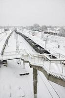 un largo tren de vagones de carga se mueve a lo largo de las vías del tren. paisaje ferroviario en invierno después de la nevada foto