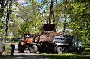 el equipo de mejora de la ciudad quita las hojas caídas en el parque con una excavadora y un camión. trabajo estacional regular en la mejora de los lugares públicos para la recreación foto