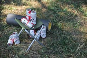 KHARKOV, UKRAINE - MAY 5, 2022 Few Cans of Budweiser Lager Alcohol Beer on fisherman chair outdoors. Budweiser is a Brand from Anheuser-Busch Inbev photo
