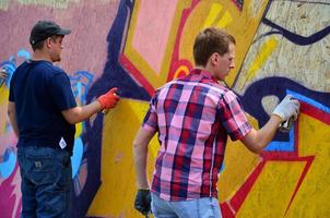 KHARKOV, UKRAINE - MAY 27, 2022 Festival of street arts. Young guys draw graffiti on portable wooden walls in the center of the city. The process of painting on walls with aerosol spray cans photo