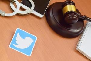 KHARKOV, UKRAINE - MAY 12, 2022 Twitter paper logo lies with wooden judge gavel, smartphone and handcuffs. Entertainment lawsuit concept photo