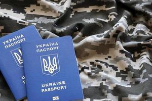 Ukrainian foreign passport on fabric with texture of military pixeled camouflage. Cloth with camo pattern in grey, brown and green pixel shapes and Ukrainian ID photo