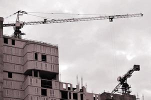 Working tall cranes inside place for with tall buildings under construction against a clear blue sky. Crane and building working progress. Retro tone photo