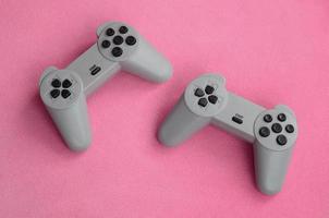 Playing games concept. Two pad joysticks lies on the blanket of furry pink fleece fabric. Controllers for video games on a background texture of light pink soft plush fleece material photo