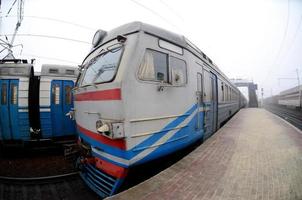 The railway track in a misty morning. The Ukrainian suburban train is at the passenger station. Fisheye photo with increased distortion