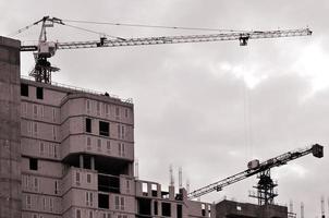 Working tall cranes inside place for with tall buildings under construction against a clear blue sky. Crane and building working progress. Retro tone photo