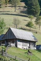 The old Ukrainian hut with a slate roof and a wooden fence in a green field photo