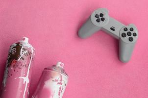 Teenagers and youth lifestyle concept. Joystick and two spray cans lies on the blanket of furry pink fleece fabric. Controllers for video games and paint cans on a plush fleece material background photo