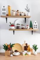 estantes de cocina de madera sobre una pared con textura blanca y parte de una encimera con utensilios ecológicos y adornos navideños. cocina de año nuevo. foto