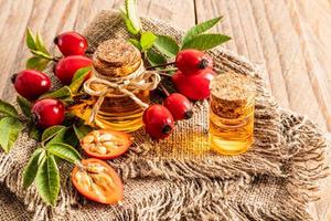 two glass bottles with a cork with an organic agent based on rosehip seed oil stand on burlap among the ripe rose hips. wooden background.