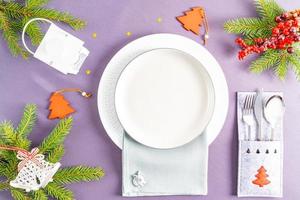vista superior de un mantel gris con platos blancos vacíos rodeados de baratijas navideñas. en la servilleta está el símbolo del año 2023 conejo o liebre.