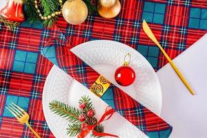 sirviendo la mesa navideña en los colores tradicionales de blanco, rojo, verde. plato blanco, cubiertos de oro. vista superior. foto