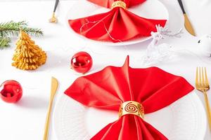 hermoso diseño moderno de la porción navideña de la mesa festiva. servilletas rojas dobladas en abanico con decoraciones en platos blancos. foto