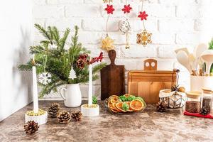 un fragmento de una parte de una cocina moderna con varias decoraciones navideñas, velas, un plato de rodajas de naranja secas. mesa de mármol. pared de ladrillo.