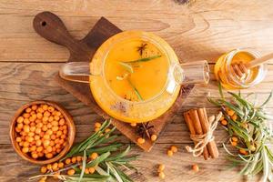 autumn composition of the tea ceremony. a large glass teapot with sea buckthorn tea, honey in a jar, berries in the bowl. top view. wooden background. photo