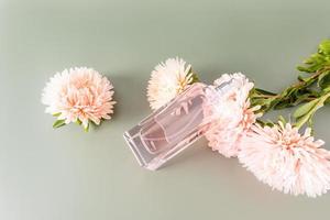 una botella de hermoso perfume de mujer o agua de tocador se encuentra sobre flores de otoño y fondo pastel. presentación de una fragancia sensual. foto