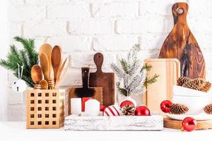 Front view of eco-friendly wooden kitchen utensils and Christmas decorations in a wooden box on a white wooden table against a brick wall. photo