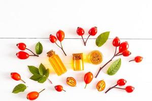 top view of several different bottles with a cork with natural rosehip seed oil. green leaves and rose hips. white background. alternative medicine. photo