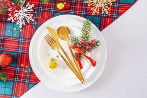 hermosa vista de la porción festiva de la mesa de año nuevo o navidad. un juego de platos blancos y cubiertos dorados con adornos. foto