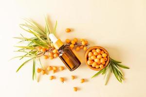 cosmetic bottle with pipette with an organic remedy based on sea buckthorn oil against of ripe berries. skin care and nutrition. top view. photo