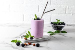 cóctel de bayas de mora o batido en vasos de vidrio modernos en forma de lata de cerveza con paja ecológica frente a una pared de ladrillo blanco. alimentación saludable. foto