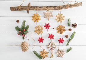 New Year's garland of wooden snowflakes on a thick wooden branch. green branches of spruce, cones. white wooden background made of boards. photo